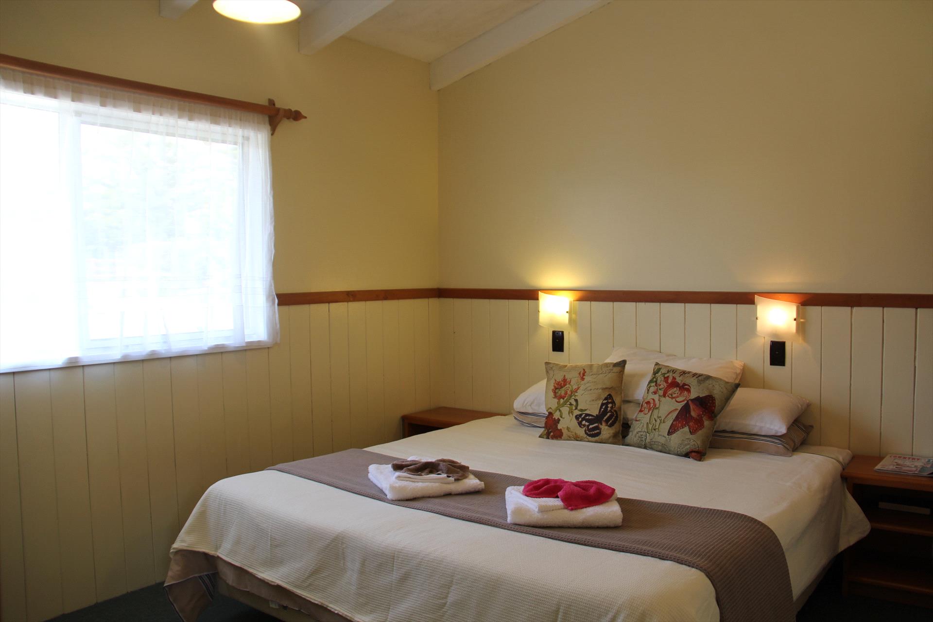 A prepared bedroom at Saints Holiday Apartments with a large bed, warm lighting and timber details